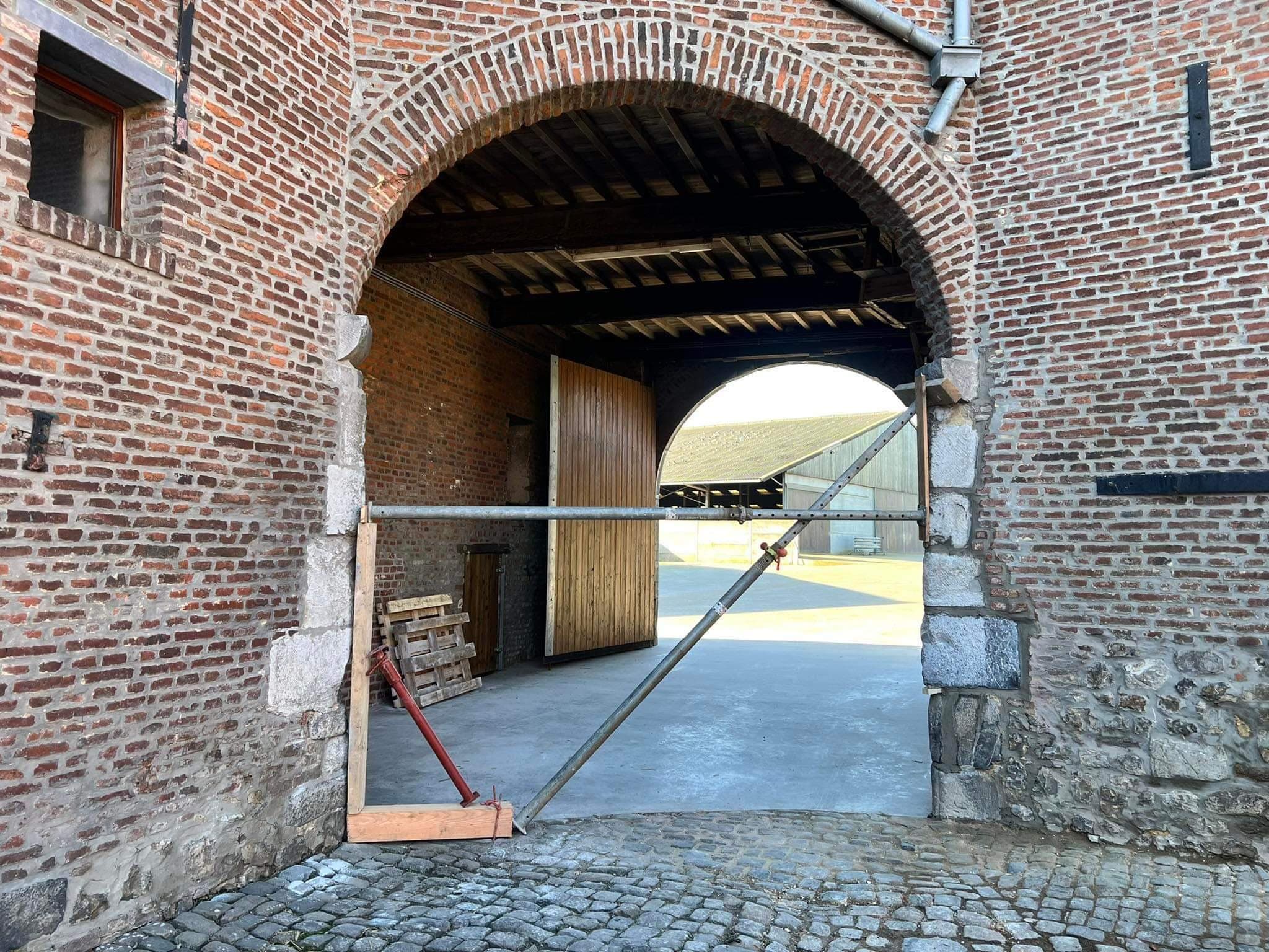 Porche voûté en briques et pierre d’une ferme en carré, ouvert sur la cour pavée